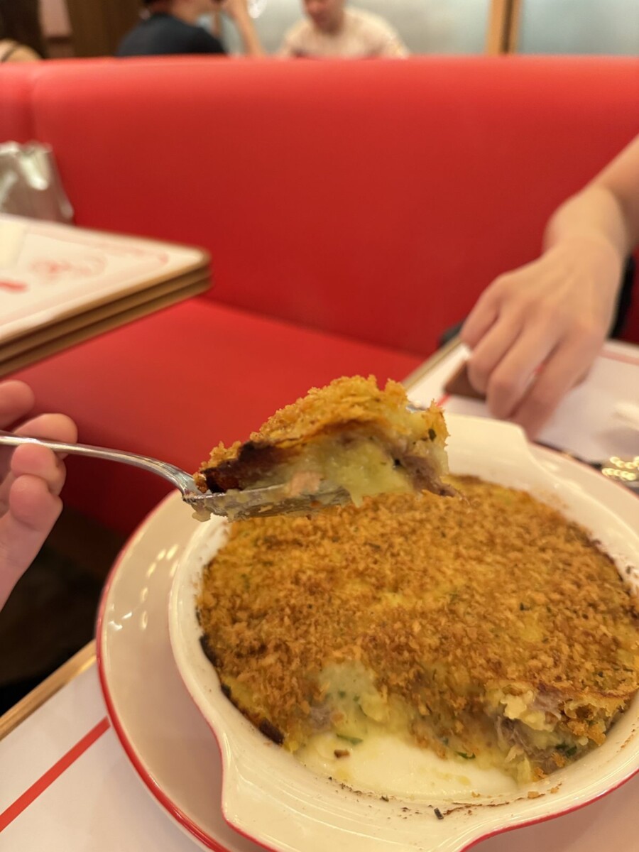 Spoonful of duck parmentier showing shredded duck confit under crushed potato