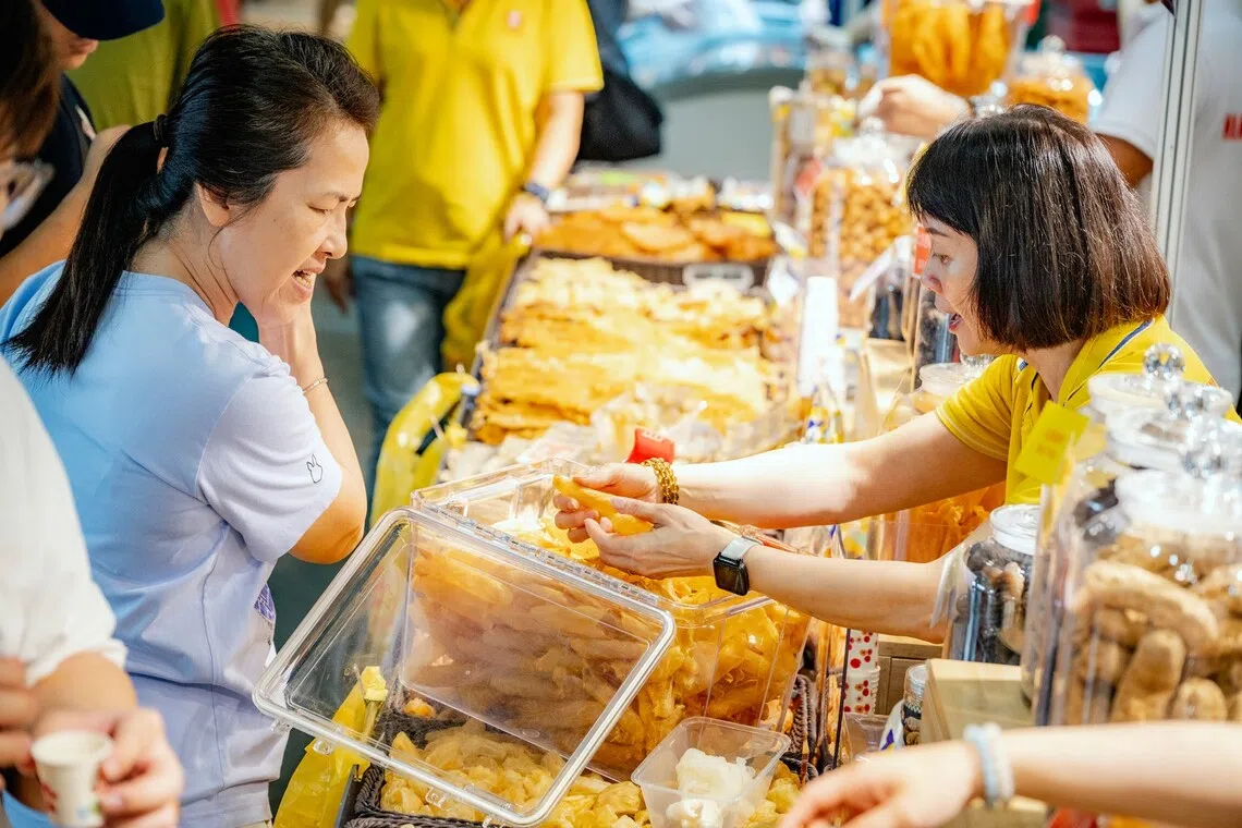 A vendor shows dried snacks to a visitor at a busy TLM Food Expo stall