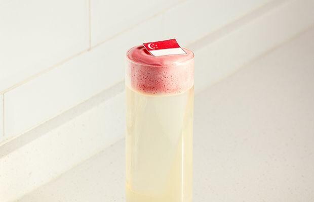 A Nutmeg & Clove cocktail topped with pink foam and a Singapore flag