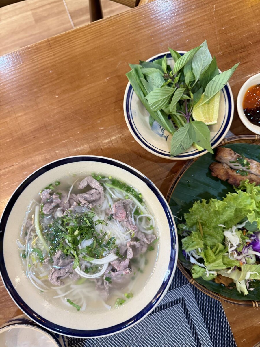 Spread of beef pho, fresh herbs and grilled spring rolls on banana leaf at A Taste of Saigon