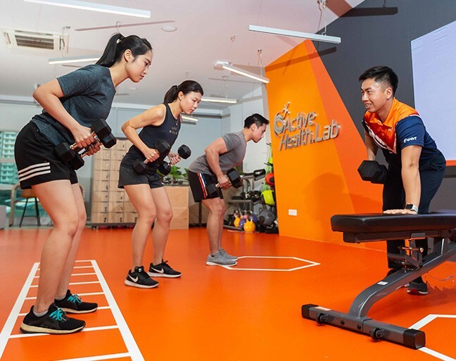 Adults doing dumbbell rows with a coach at an ActiveSG Active Health Lab