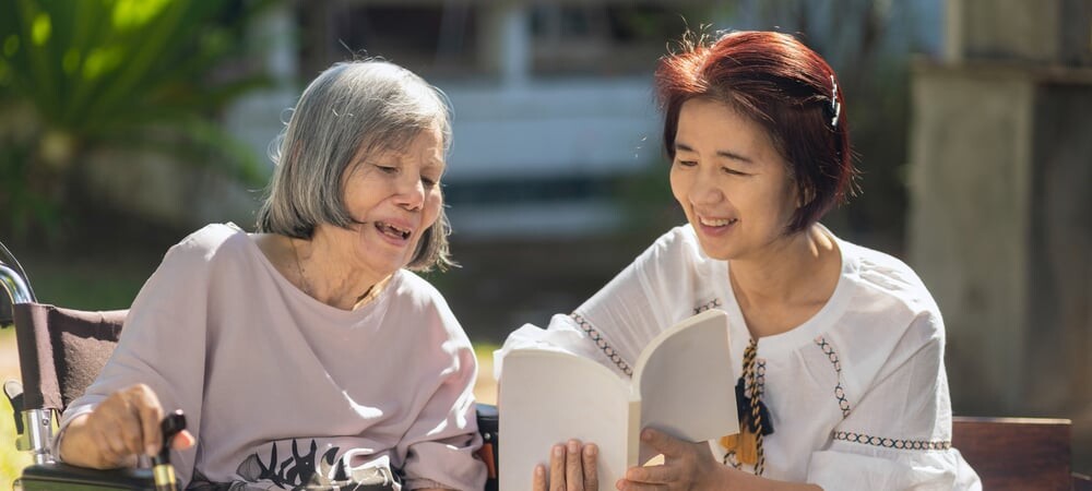 A volunteer reads with an older woman in a wheelchair