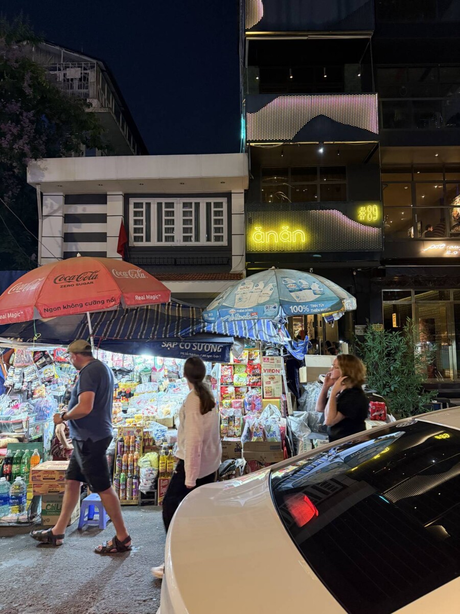 Entrance to Anan Saigon Michelin restaurant at night, yellow neon sign above wet market stalls in District 1