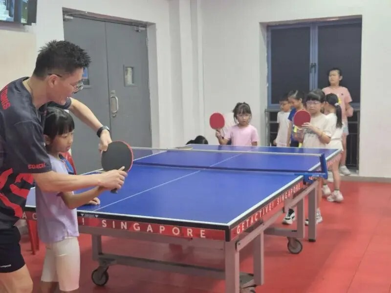 ActiveSG coach guiding a child at table tennis while other children wait their turn