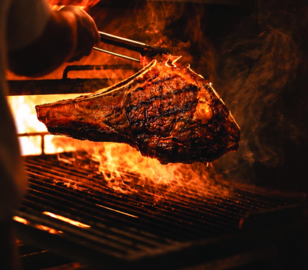A bone-in steak cooking over open flames on the grill at Barossa Steak & Grill
