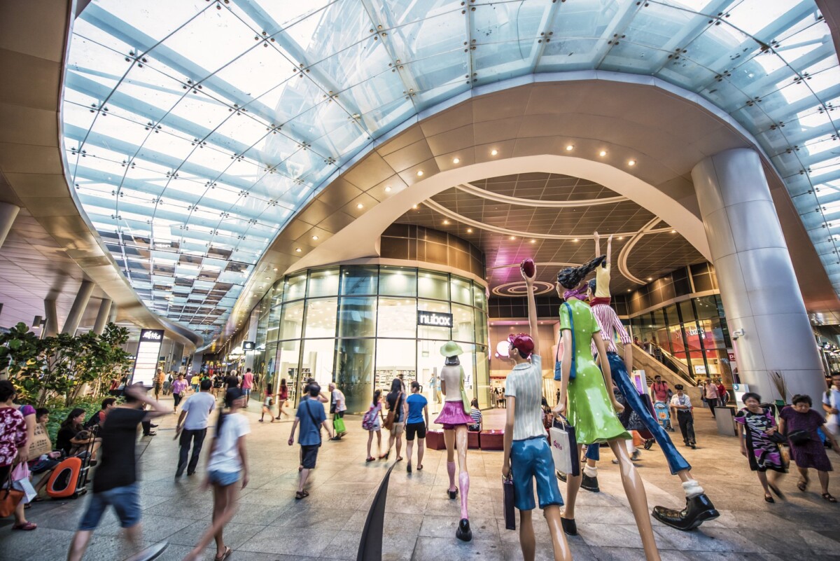 Shoppers walking past the family sculptures under the glass canopy at the Bedok Mall entrance