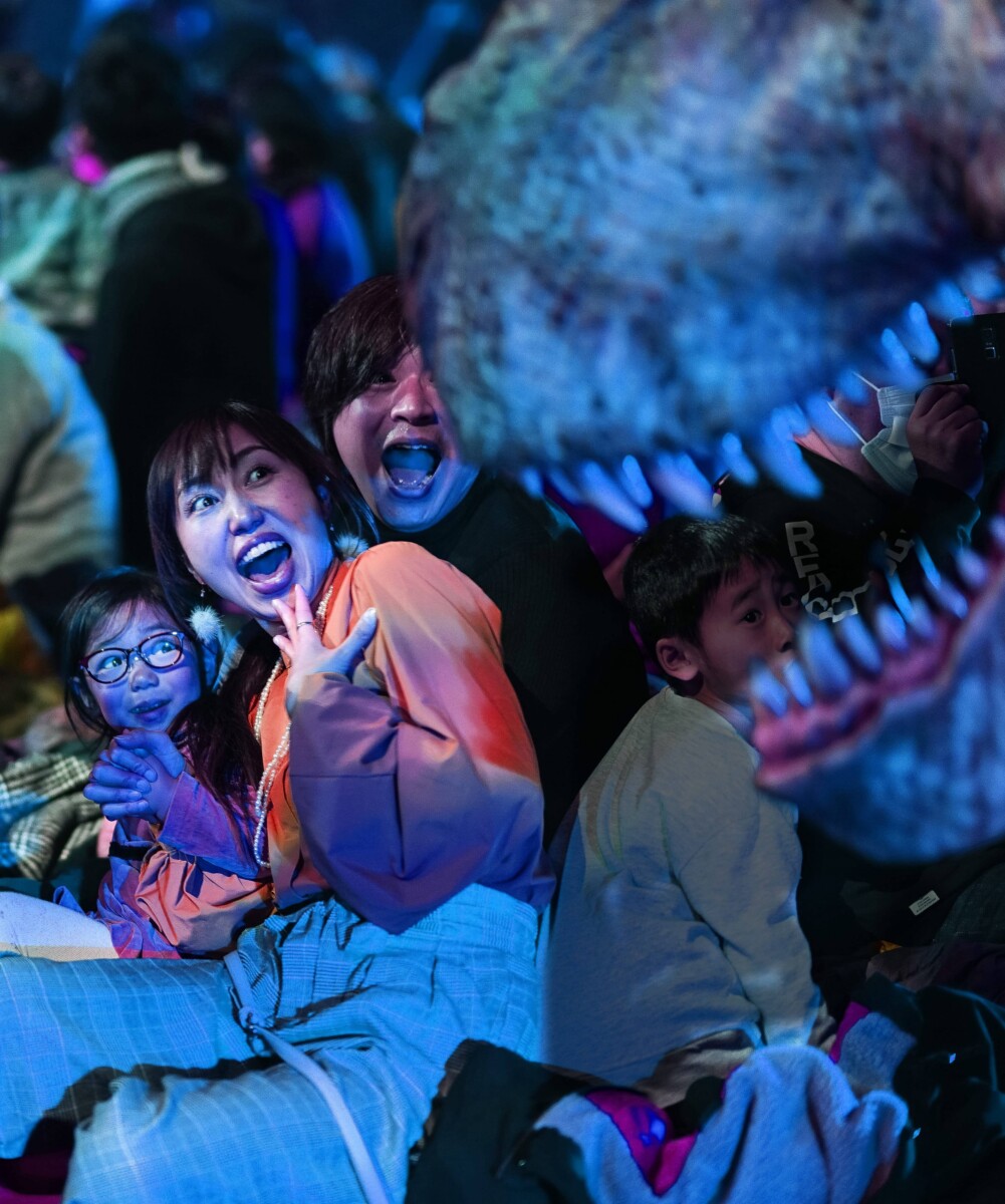 Children react as a dinosaur leans over the audience