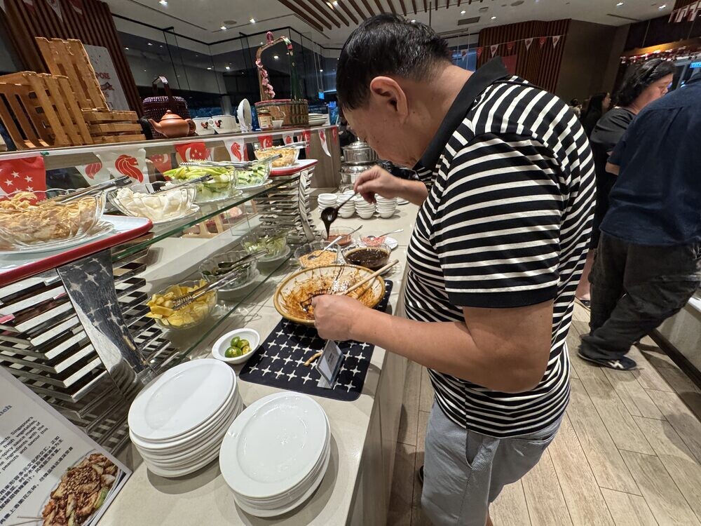 Kevin in a striped polo shirt assembling his own rojak at the DIY station, plates stacked beside him