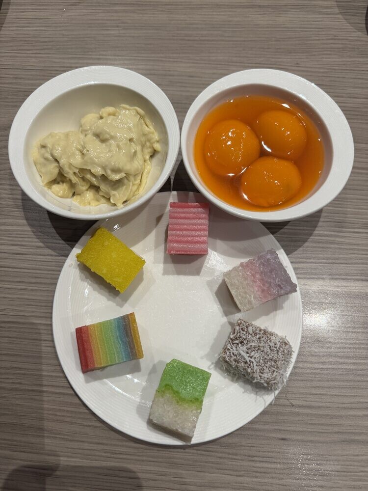 Dessert plate with Durian Pengat in a bowl, a second pale dessert, and assorted kueh in pink, green and rainbow layers