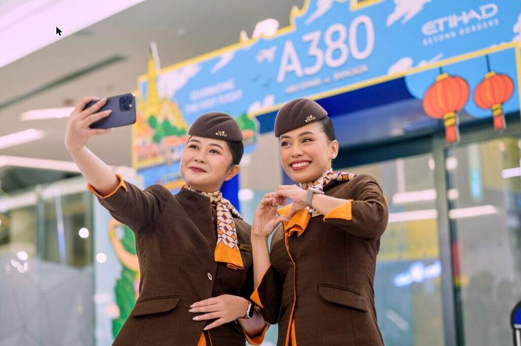 Etihad cabin crew taking a selfie in front of the A380 first flight backdrop in Bangkok