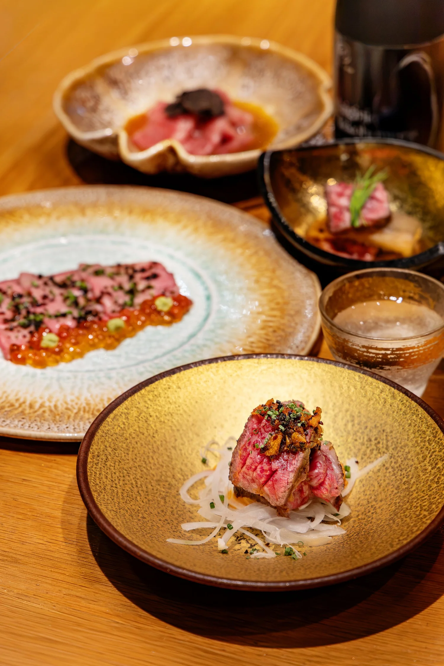 Fat Cow 15th anniversary wagyu courses laid out with sake glasses and a bottle