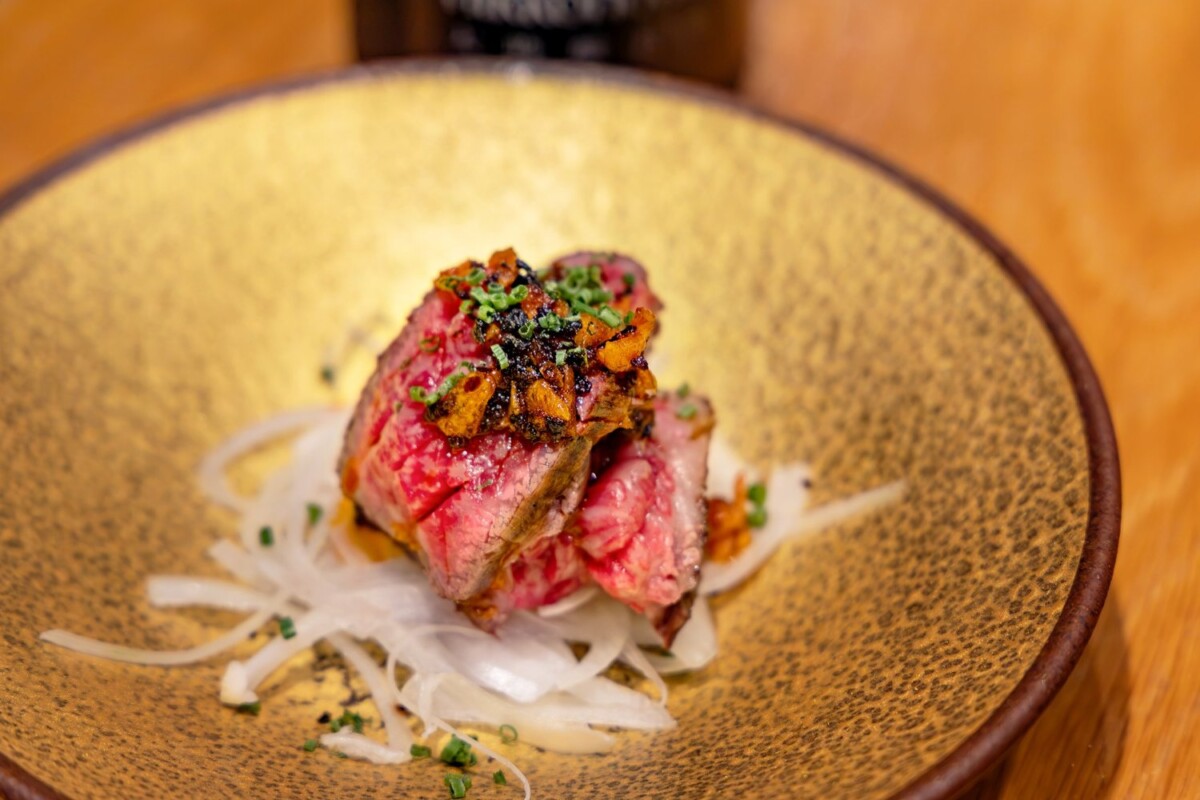 Straw-seared wagyu inside skirt on sliced onion with garlic chips and chives at Fat Cow