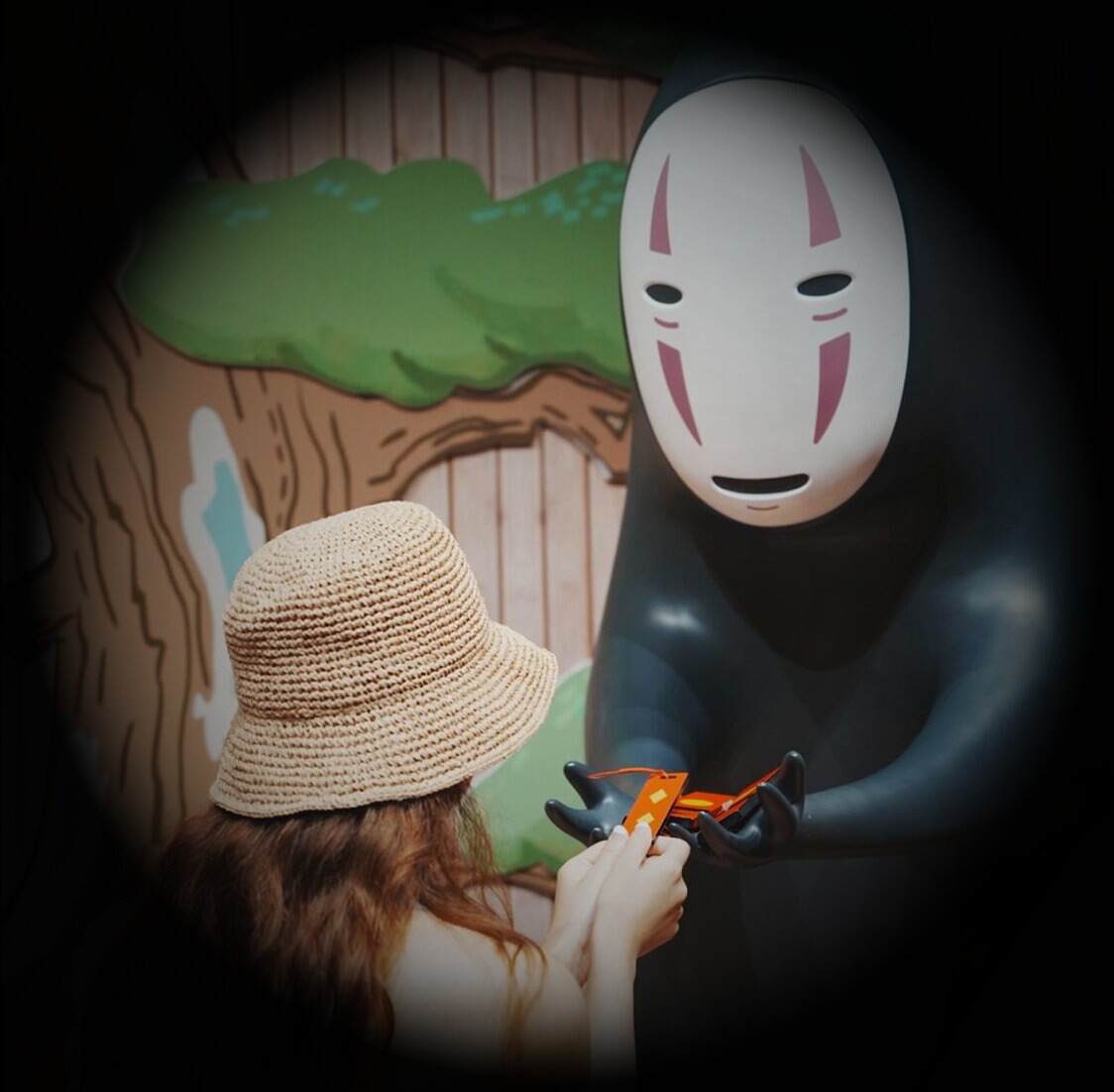 A visitor in a straw hat facing a life-size No Face figure
