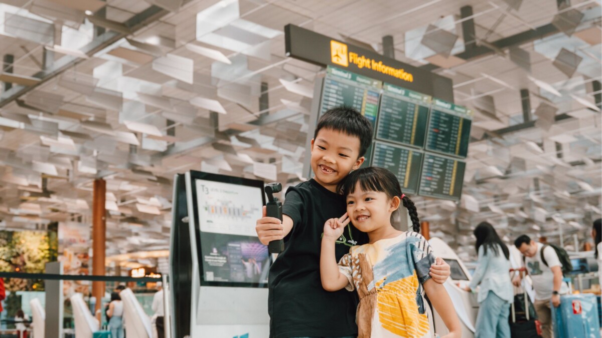 Two children take a selfie in front of the flight information board at Changi Airport Terminal 3