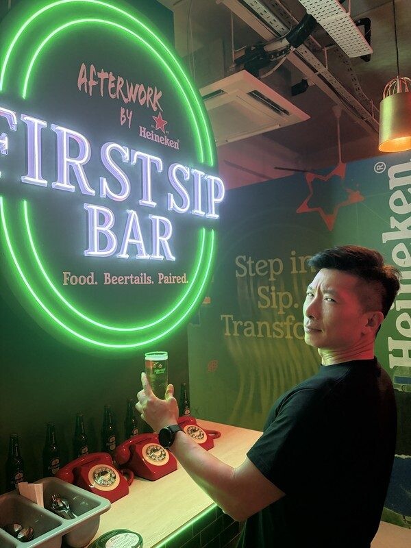 Willie posing with a Heineken can in front of the First Sip Bar neon at Heineken First Sip House