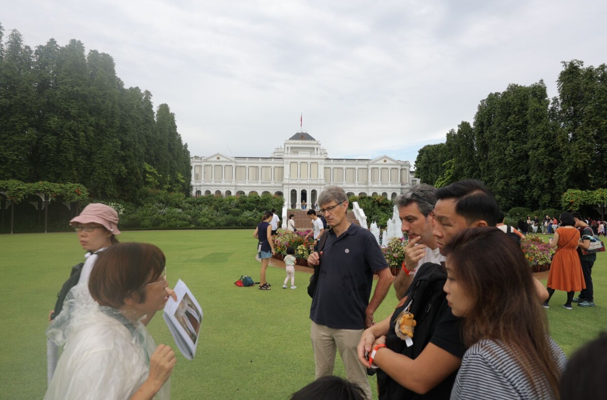 A guide leads a tour group across the Istana lawn with the main building behind