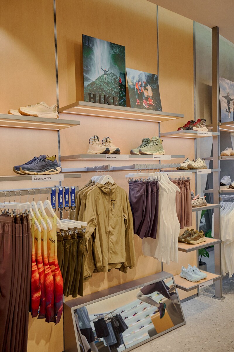 Wooden shelves of HOKA hiking shoes above racks of apparel in the Jewel store