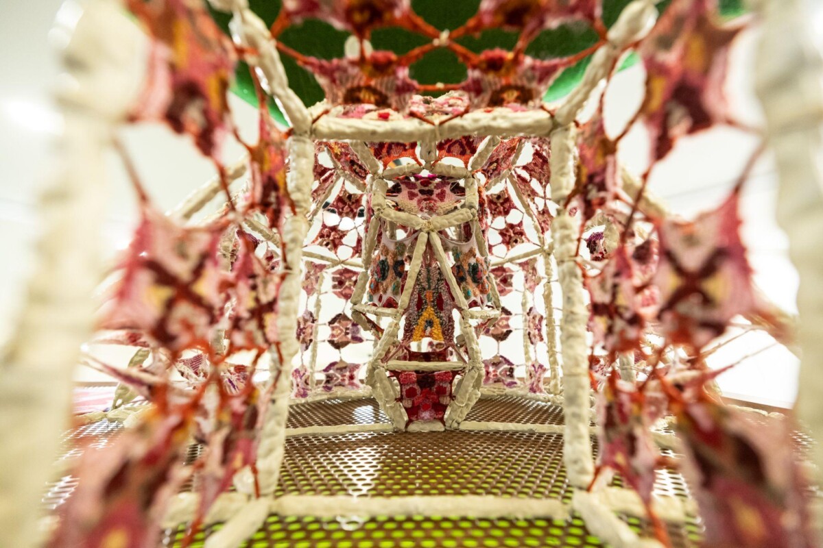 Detail view looking through the white lattice frame of a HOYA tower at the pink and red knitted panels stretched inside it