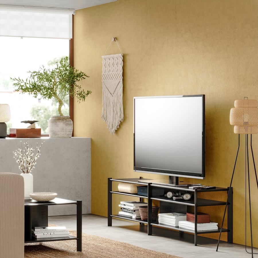 Black IKEA JÄTTESTA TV bench in a living room with a peach sofa, plant and shelves