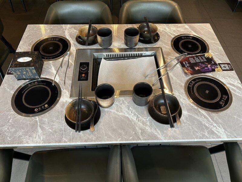 Central grill plate with parchment paper and individual induction hotpots at JING Halal Hotpot and Grill