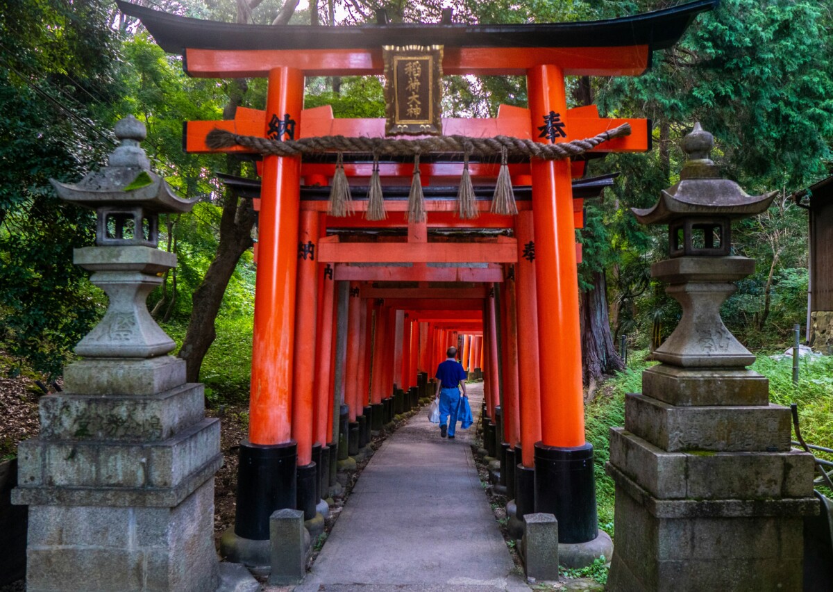 The iconic red torii gates of Fushimi Inari Shrine in Kyoto, Japan, with a visitor walking through