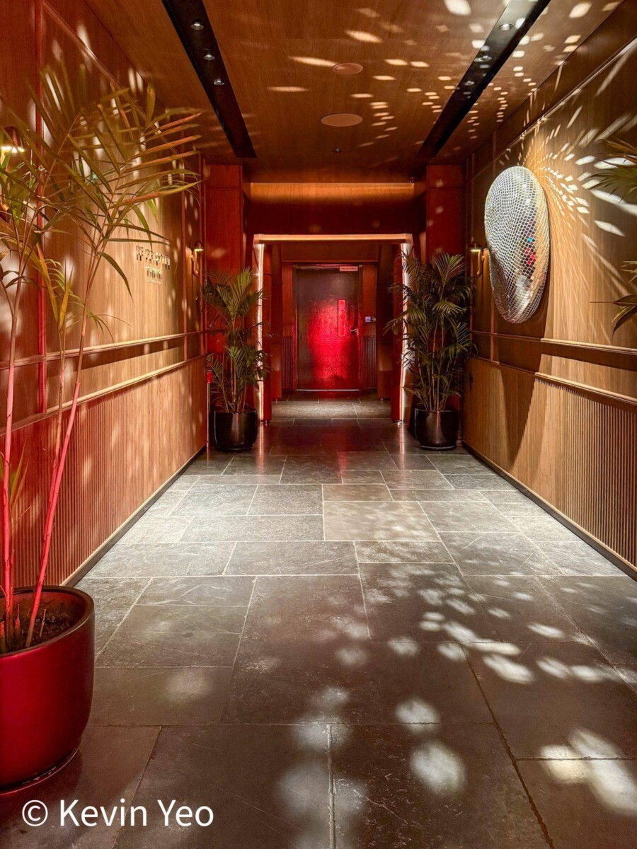 Entrance hallway at Le Pristine Singapore with potted plants leading to a red-lit doorway