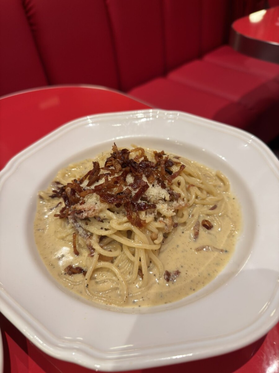 Spaghetti carbonara sitting in a pool of pale yellow cream with crispy guanciale