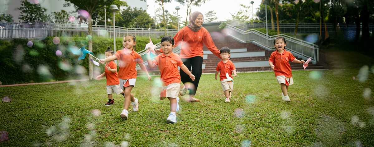 My First Skool children and a teacher running outdoors in orange uniforms