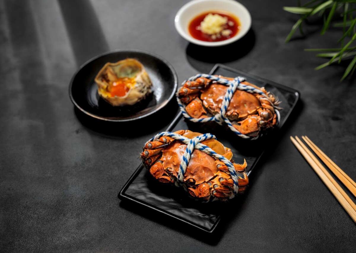 Two steamed hairy crabs tied with string and a crab shell with roe at Min Jiang