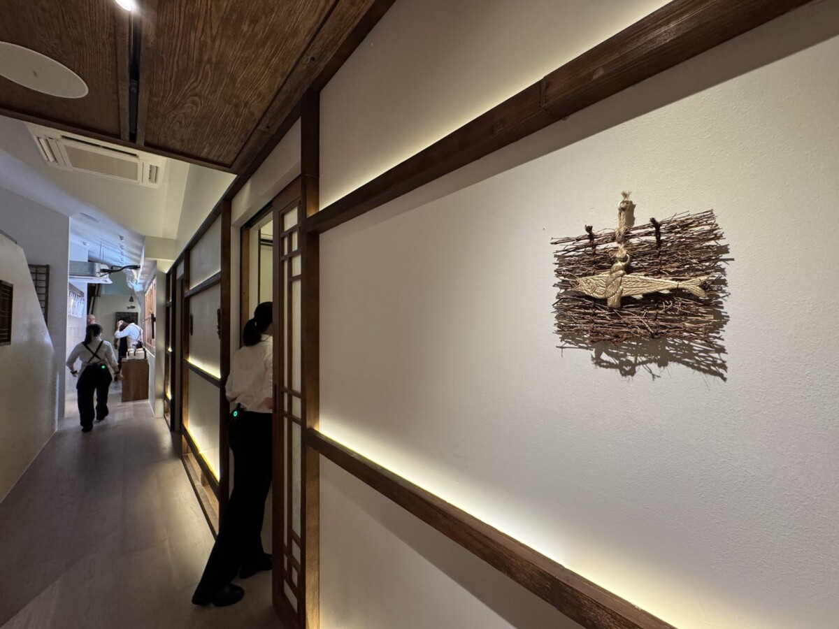 Lattice-screened corridor at MODU Samgyetang with a sculptural brass fish wall piece on twigs