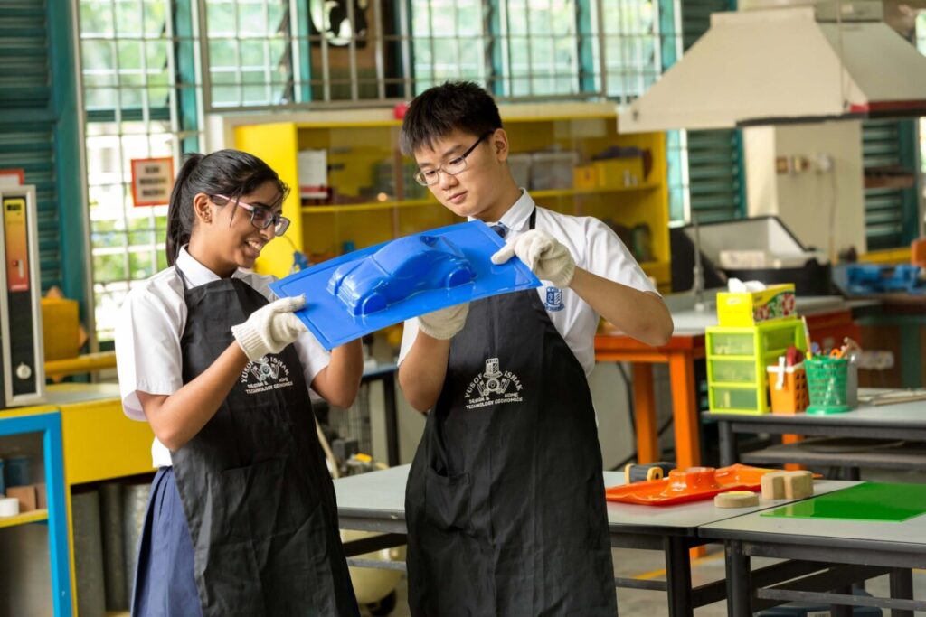 Two secondary school students in aprons holding a blue moulded part in a workshop