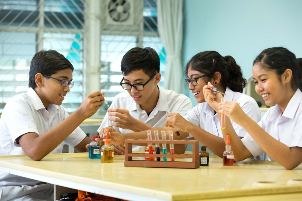 Four secondary school students in white uniforms using test tubes in a science lesson
