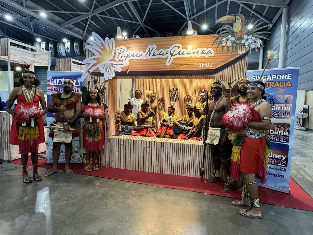 Papua New Guinea performers in feathered headdresses and red skirts posed at their Papua New Guinea booth 3H02