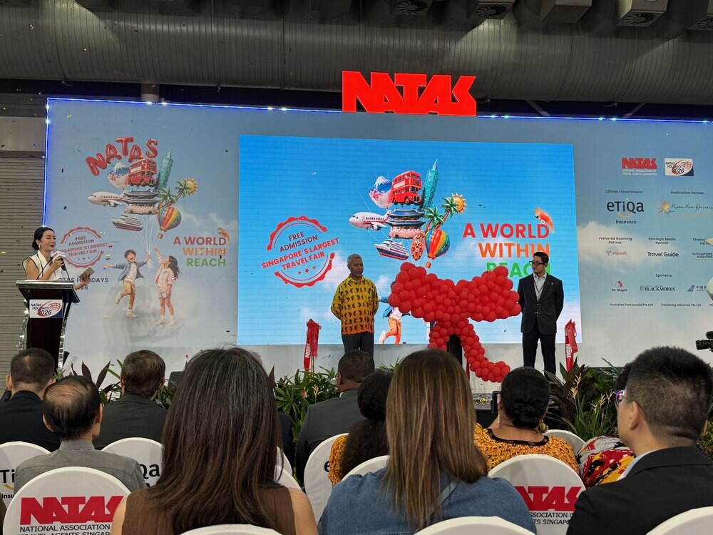 NATAS Holidays 2026 opening ceremony stage with a ribbon-cutting balloon sculpture, a screen reading Free Admission Singapore's Largest Travel Fair, and dignitaries beside it
