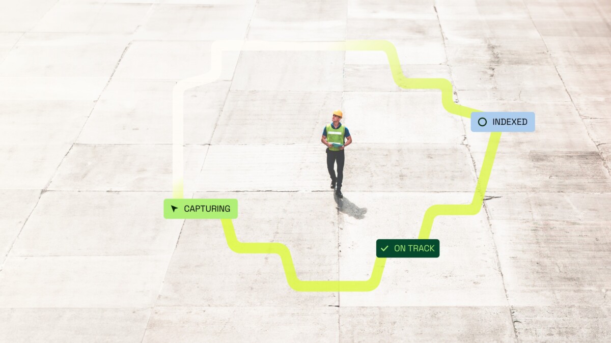 A worker in a hard hat and safety vest walking a site floor as a capture path is tracked on screen