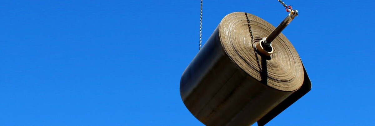 A bulk roll of Concrete Canvas cementitious mat lifted by crane chains against a blue sky