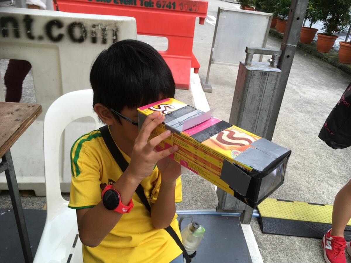Child looks through a handmade cardboard camera obscura during an Objectifs children's workshop