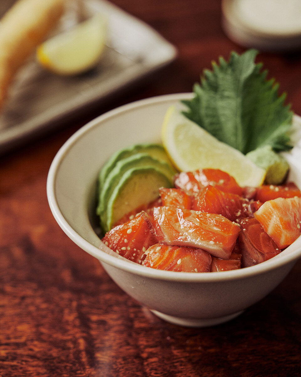 Ojeje salmon donburi rice bowl topped with avocado slices, lemon and a green leaf