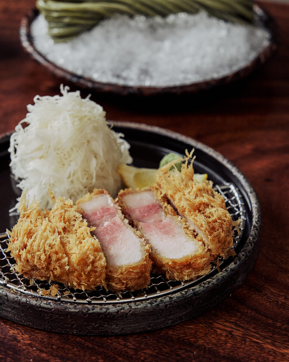 Sliced Ojeje pork tonkatsu on a wire rack with shredded cabbage and lemon