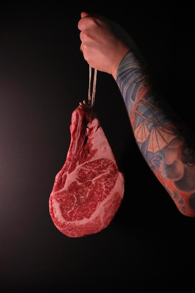 Raw marbled bone-in beef cut held up for Origin Grill's Meat Series dry-aged beef dinner