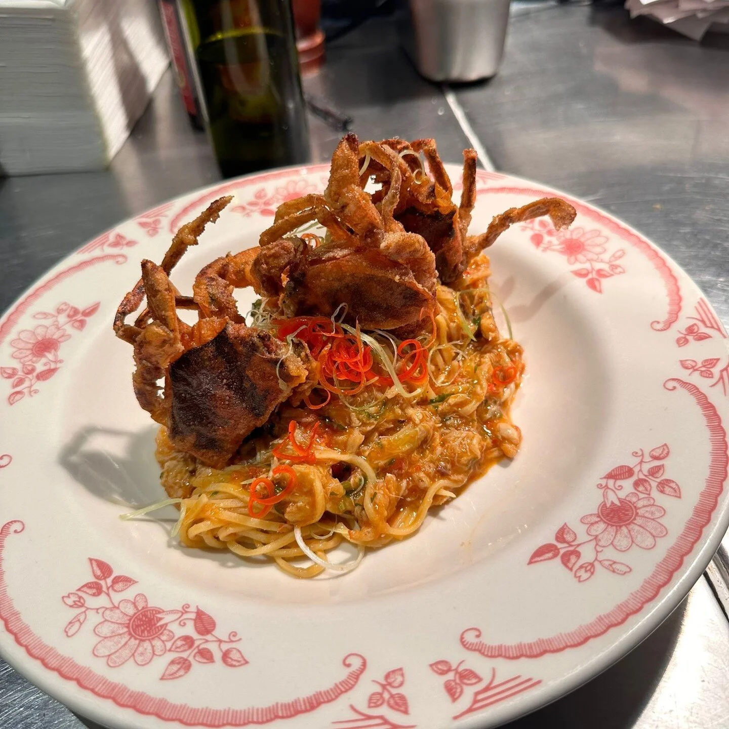 Soft shell crab on tomato pasta in a floral-rimmed plate