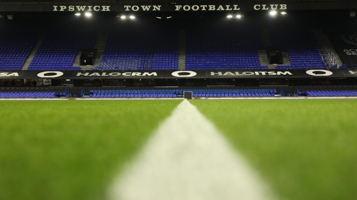 Empty blue stands at Portman Road under floodlights with Ipswich Town Football Club signage