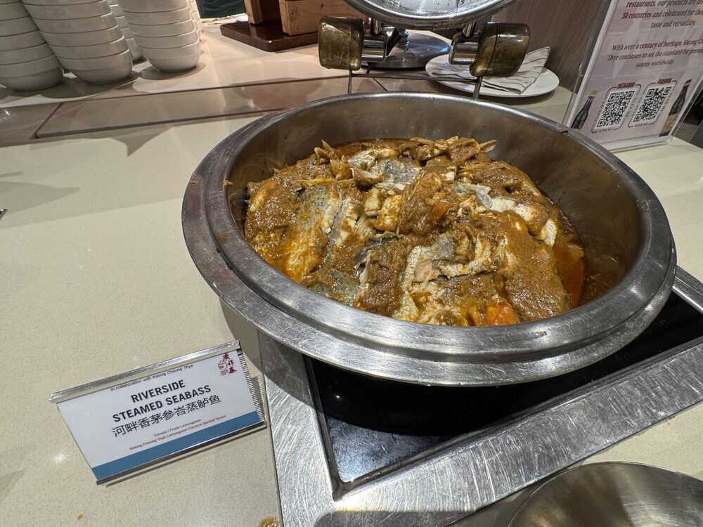 Riverside Steamed Seabass in a chafing dish with vegetables and gravy, dish label in the foreground