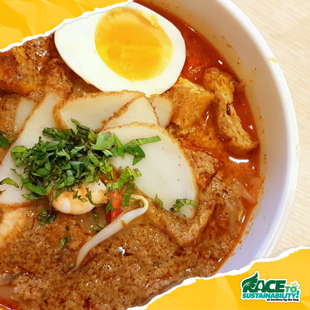 Bowl of laksa topped with egg, fishcake and prawn
