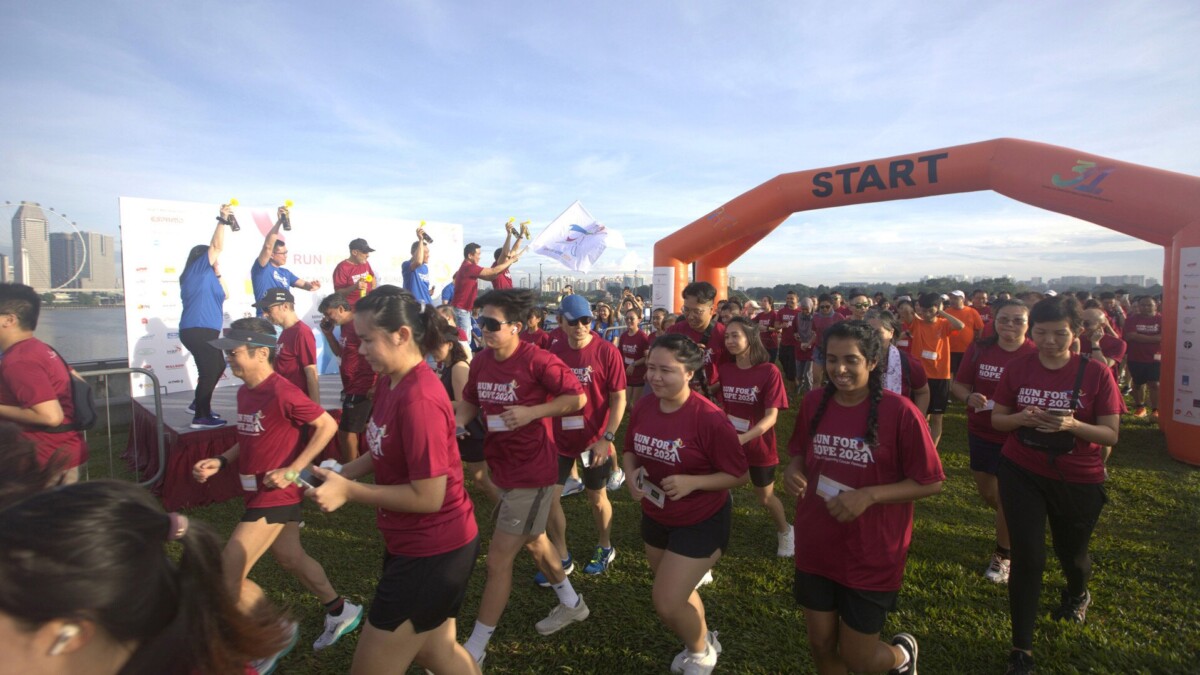 Runners in maroon Run For Hope 2024 shirts leaving the orange start arch