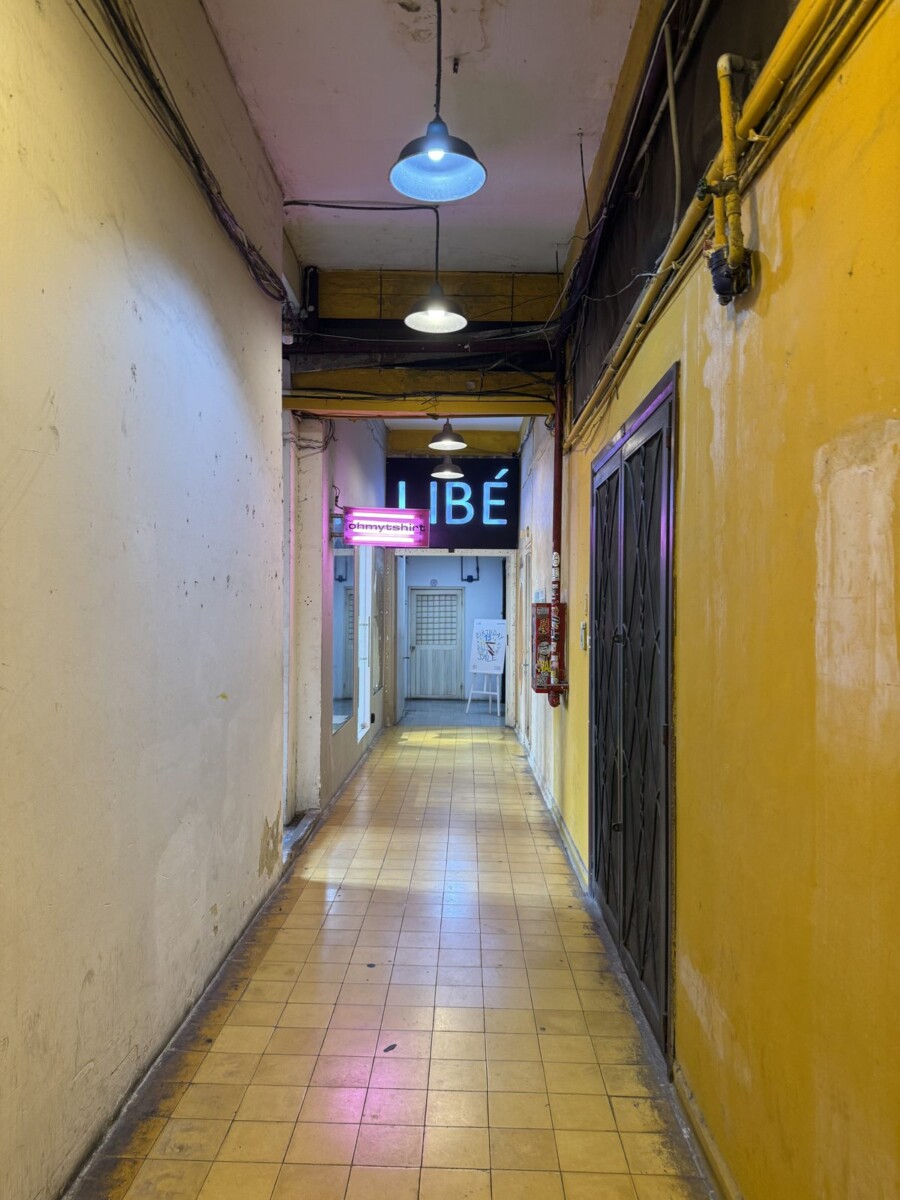 Dim corridor inside 26 Ly Tu Trong Saigon with neon signs for boutiques like LIBE and ohmytshirt at the end
