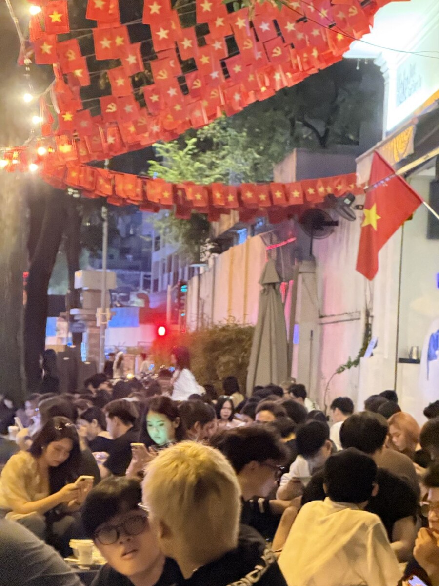 Sea of young people in a narrow Saigon lane lined with Vietnamese flags overhead