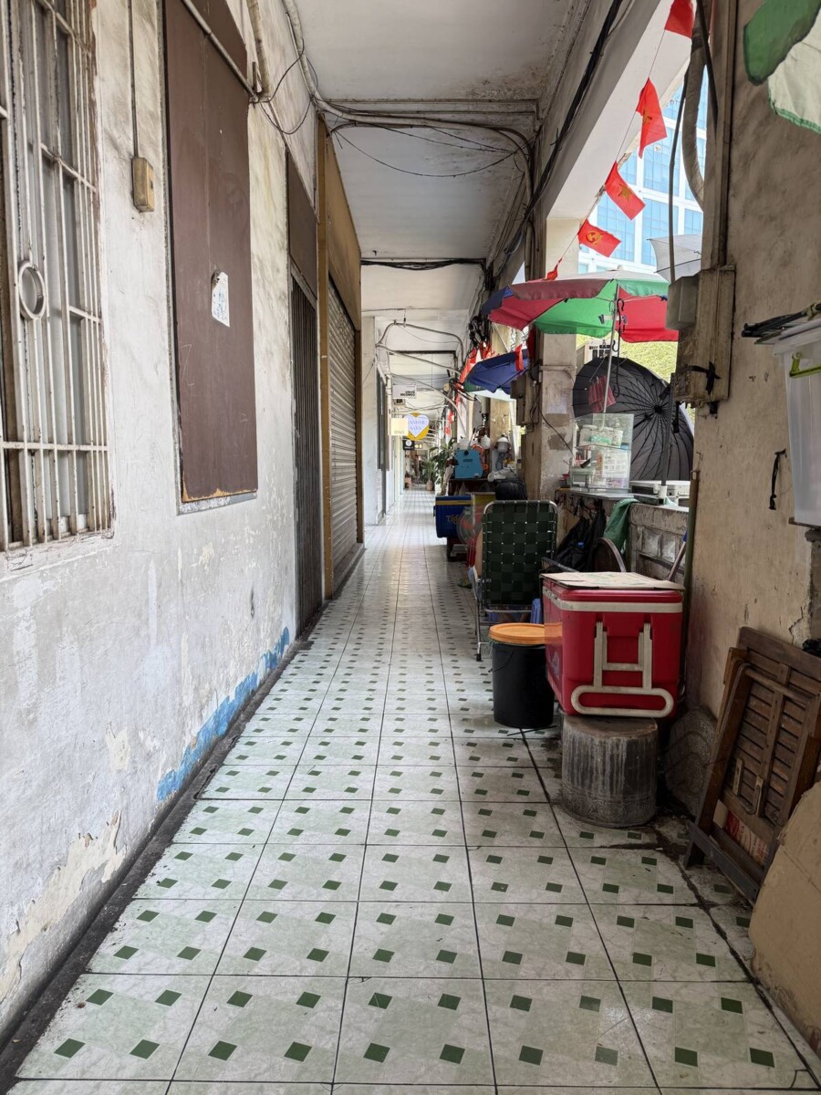 Tiled corridor of an old Saigon shophouse with peeling walls and original residential shutters, some units still occupied by residents
