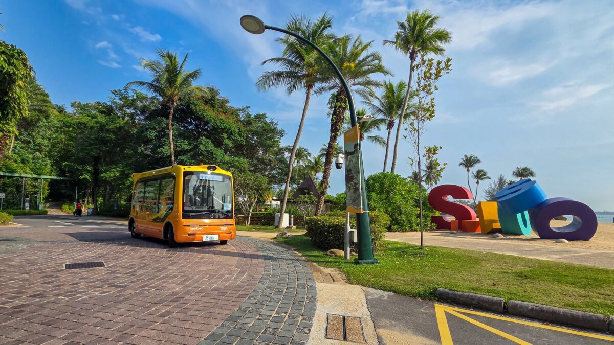 Yellow WeRide autonomous shuttle driving past the colourful Sentosa letters by Siloso Beach