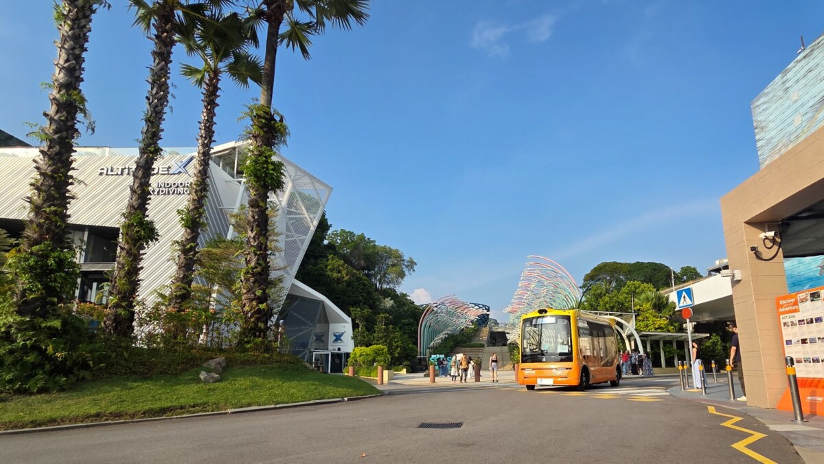 WeRide autonomous shuttle on a palm-lined road beside a Sentosa attraction building